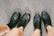 Two pairs of legs are visible, each wearing black leather shoes. One pair is wearing lace-up boots, while the other is wearing slip-on ankle boots. The ground is made of rough, textured concrete.