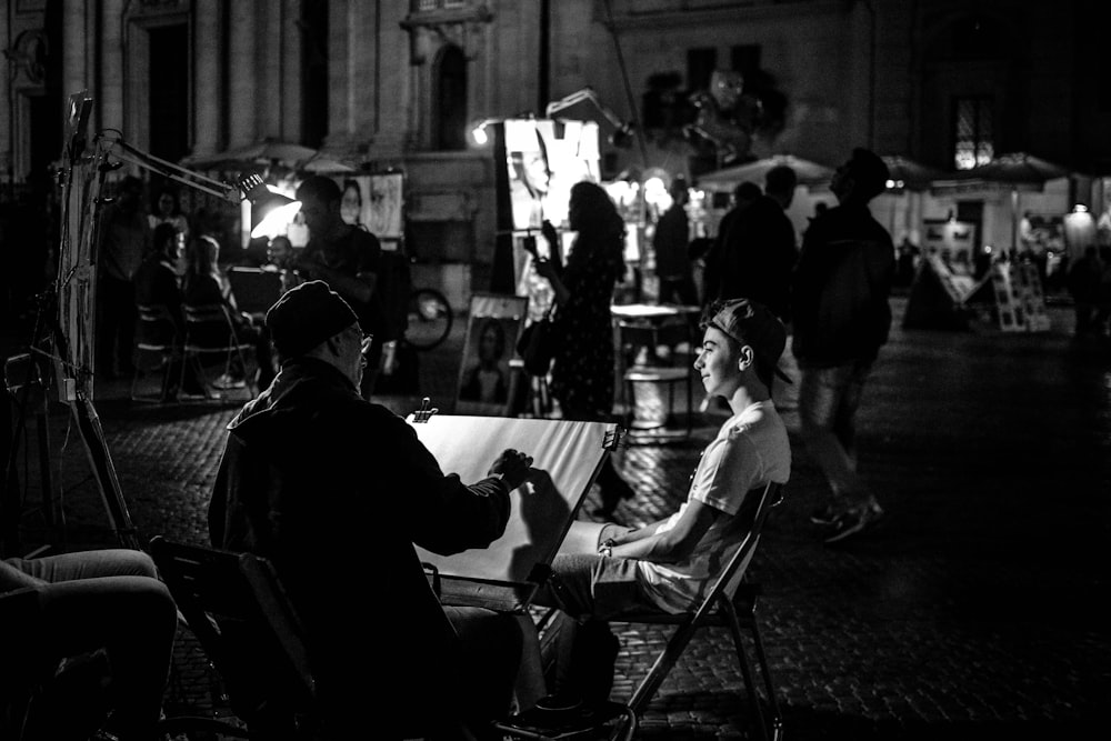 Photographie en niveaux de gris de personnes dans la rue près des bâtiments pendant la nuit