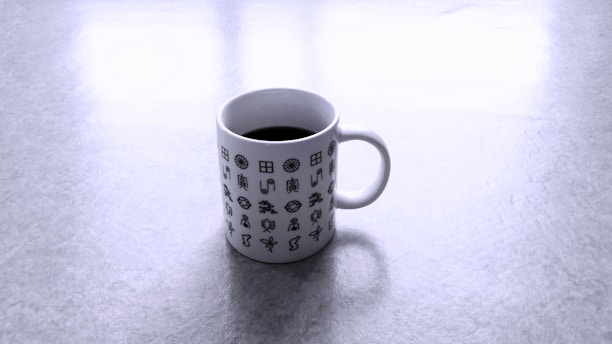A white coffee mug printed with various black geometric and abstract symbols sitting on a light gray surface.