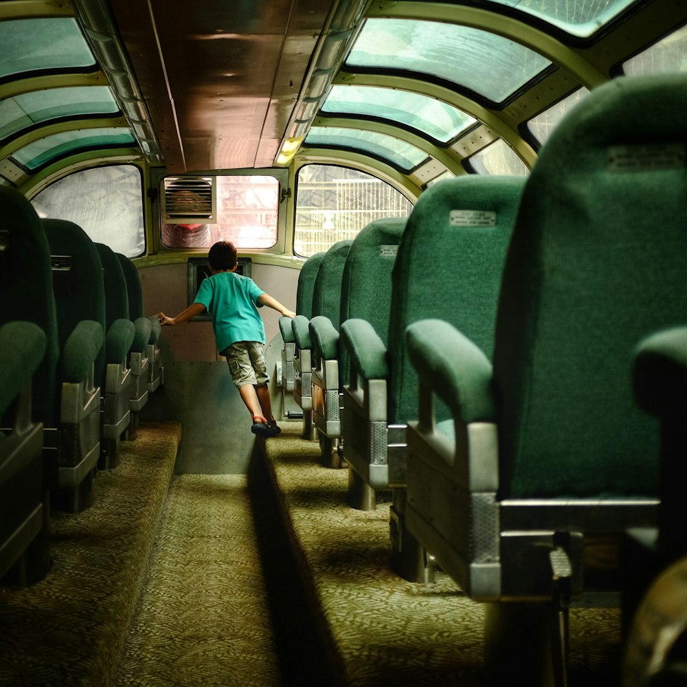 garçon marchant à l’intérieur d’un bus avec des sièges verts