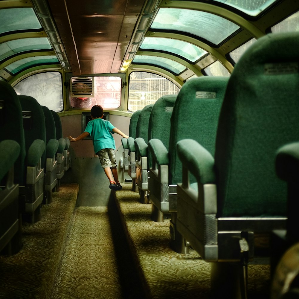 boy walking inside bus with green seats