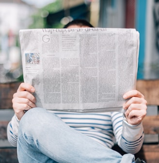 man sitting on bench reading newspaper