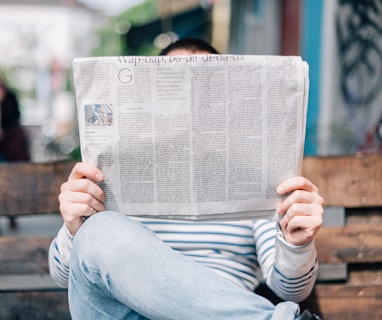 man sitting on bench reading newspaper