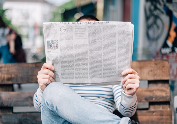 man sitting on bench reading newspaper