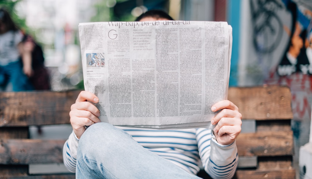 man sitting on bench reading newspaper