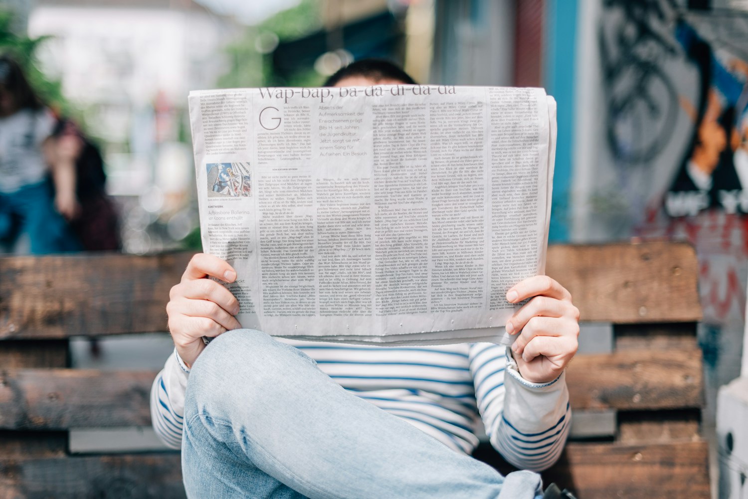 man sitting on bench reading newspaper by Roman Kraft