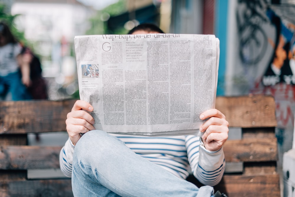 Mann sitzt auf Bank und liest Zeitung