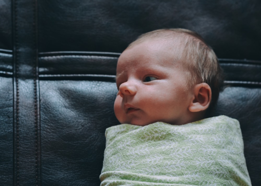 bébé recouvert d’une couverture verte sur une surface en cuir noir