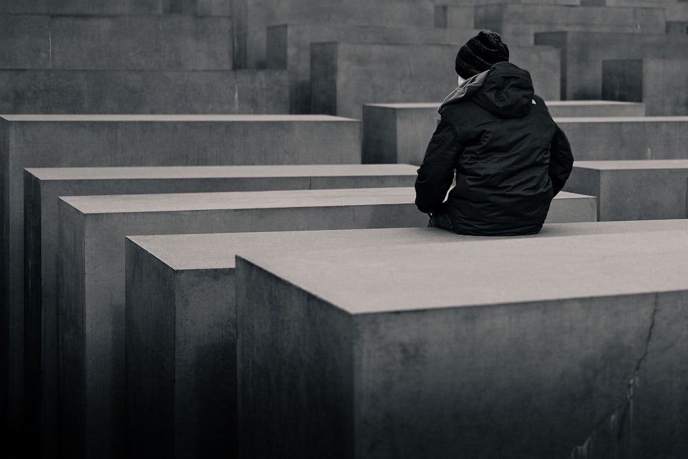 grayscale photo of woman sitting on concrete block
