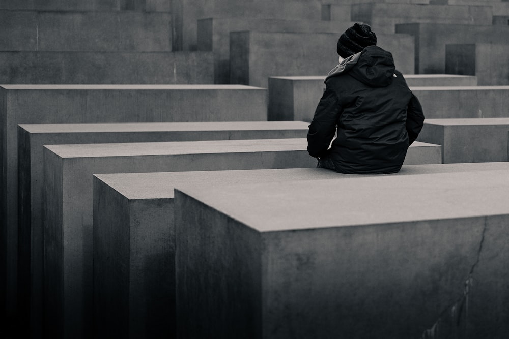 Photo en niveaux de gris d’une femme assise sur un bloc de béton