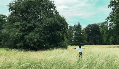 A person standing barefoot on green grass, arms outstretched to the breeze.