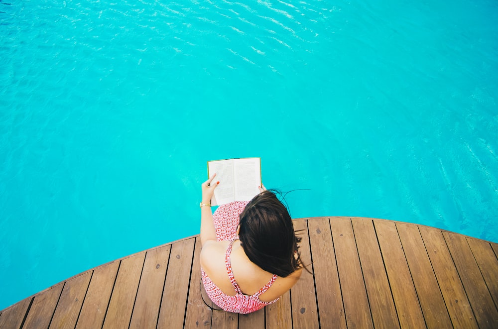 Frau sitzt auf Dock am Pool, während sie reitet Buch
