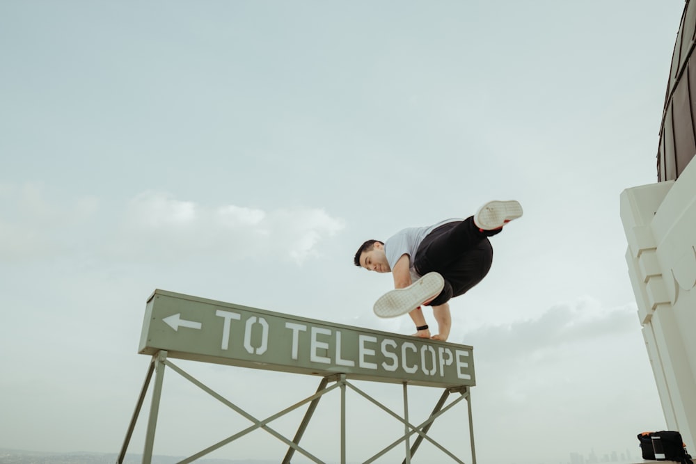 man jumping over to telescope signage
