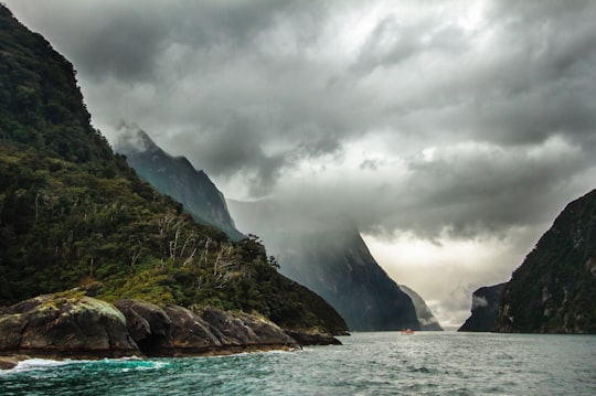 peak of mountain covered with clouds near body of water in Milford Sound New Zealand