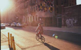 A rider cruising an Exploit e-bike along a sunlit city street with colorful murals.