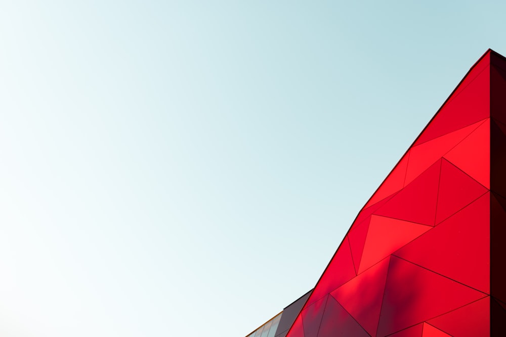 밝은 빨간색의 삼각형 건물 꼭대기가 보이는 하늘색 하늘