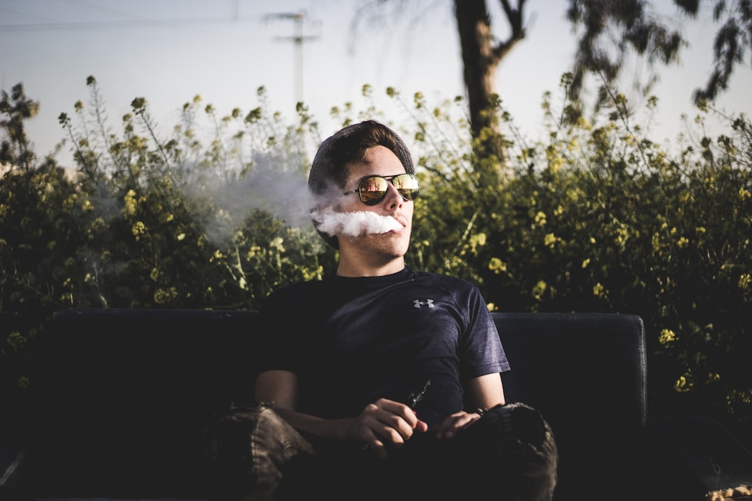 Un homme assis sur un banc dans la nature, fumant une cigarette électronique