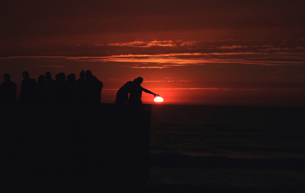 Silueta de la gente de pie en la playa durante la puesta del sol