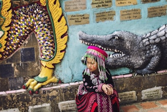 girl wearing multicolored traditional dress sitting near the wall