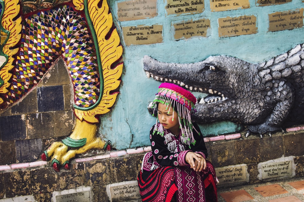 여러 가지 빛깔의 전통 드레스를 입은 소녀 벽 근처에 앉아