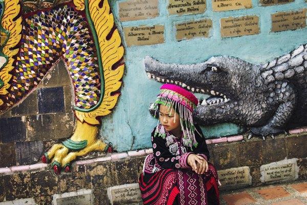 Girl wearing multicolored traditional dress sitting near the wall — Chiang Mai, Thailand