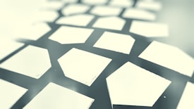 Geometric shapes form a pattern resembling a honeycomb or grid, with a mix of curved and straight edges. The design appears abstract and is presented in a monochromatic color scheme.