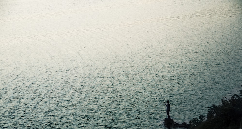 person stand on rock near body of water during daytime