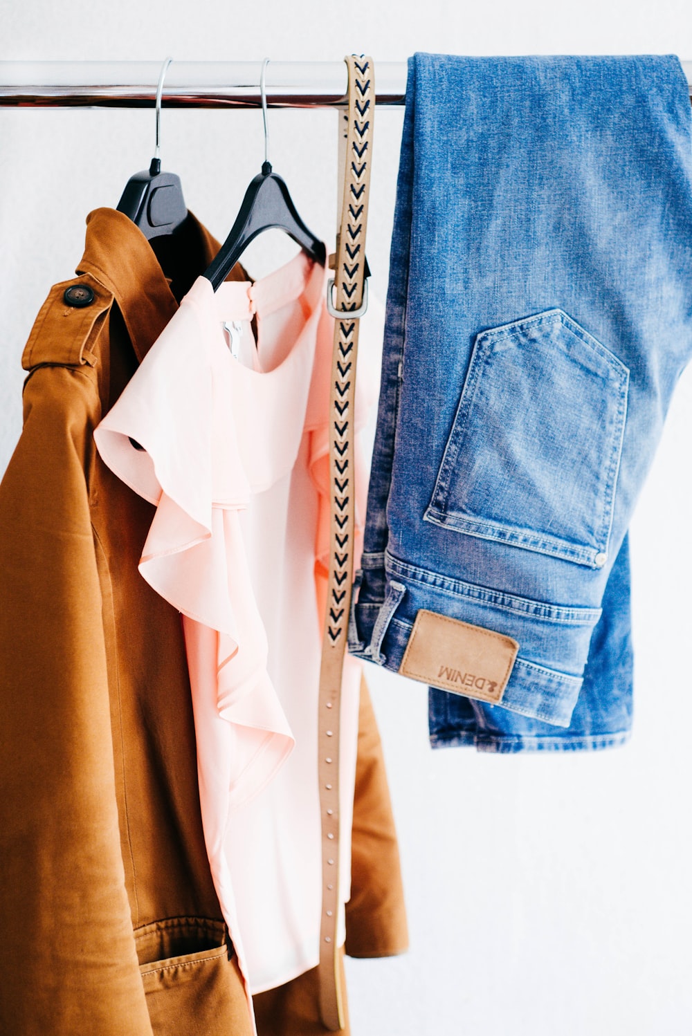 Women's shirts, jeans, and belt hanging on a clothing rack