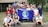 A group of young people gathered together outdoors in front of a building, holding a blue flag with the Earth on it and the words 'PHS Global Ecology.' The group appears cheerful and diverse, standing closely together.