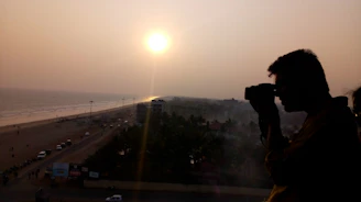 A warm sunset over Vizag’s coastline with a silhouette of a photographer capturing the scene.