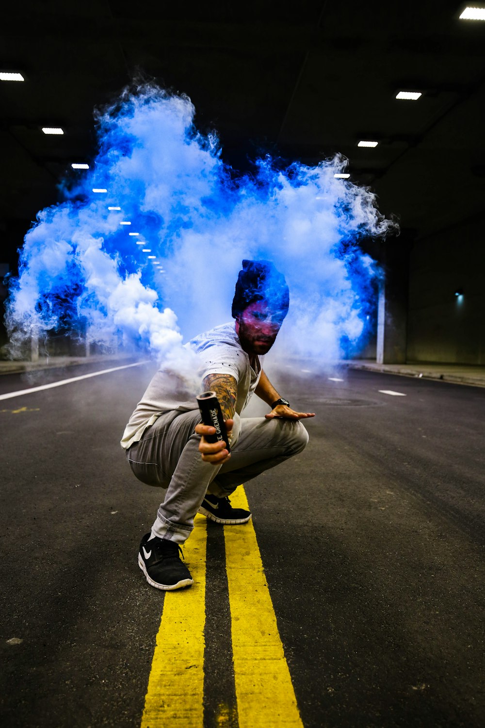 Homme tenant un tube noir avec de la fumée bleue au milieu de la route