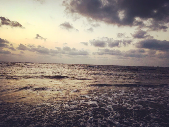 A calm sea at dusk, charcoal clouds reflecting gently on the water’s surface.
