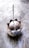 A lit incense stick is placed in an ash-filled, dome-shaped incense holder with a lotus petal design on a textured stone surface. Wisps of smoke gently rise from the incense, creating a subtle, calming atmosphere.