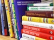 A collection of business and motivational books on a shelf, featuring titles like 'Greening Your Business,' 'Billions of Entrepreneurs,' 'Great Again,' and 'Higher Ambition.' The books are arranged vertically, showing a variety of colors and sizes.