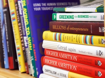 A collection of business and motivational books on a shelf, featuring titles like 'Greening Your Business,' 'Billions of Entrepreneurs,' 'Great Again,' and 'Higher Ambition.' The books are arranged vertically, showing a variety of colors and sizes.