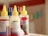 Several bottles with yellow caps are arranged closely together. The bottles have labels with text and colorful designs, and contain what appears to be ink or dye. The surroundings are blurred, suggesting a shallow depth of field.