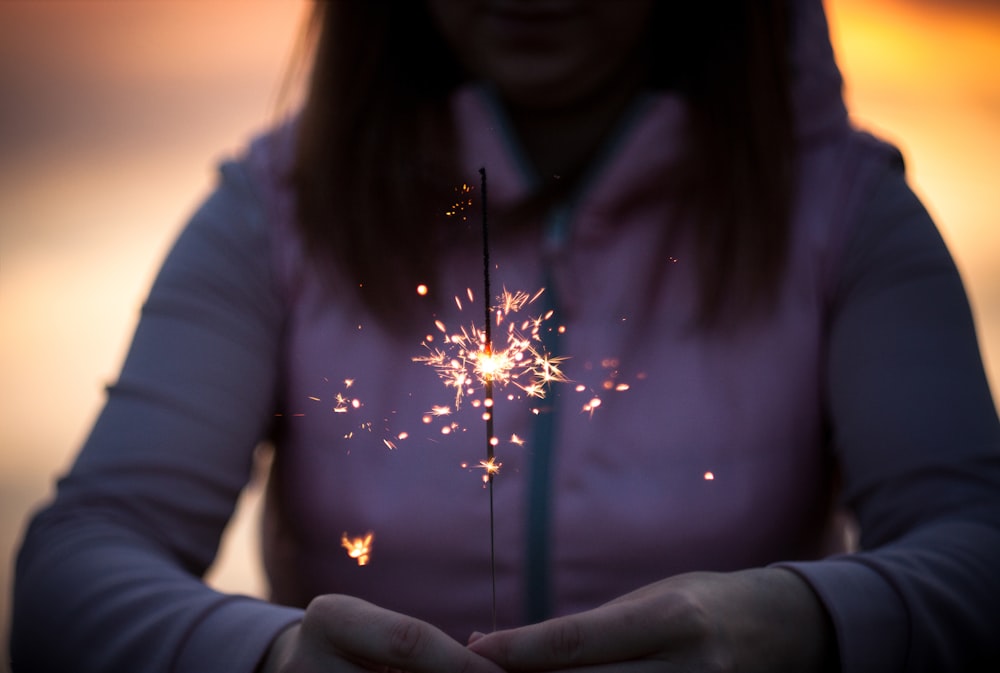 A woman in a hoodie holds a lit sparkler in her hands