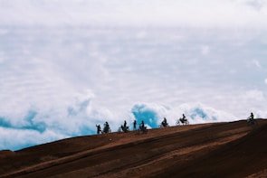 A group of riders on big trail motorcycles taking a break on a dirt path under bright sunlight.