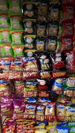 A display rack filled with various flavored snack packets, mainly chips from brands like Lay's and Kurkure, arranged in a colorful and visually appealing manner.