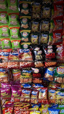 A display rack filled with various flavored snack packets, mainly chips from brands like Lay's and Kurkure, arranged in a colorful and visually appealing manner.