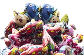 A vibrant collection of colorful foil balloons featuring various cartoon characters, including fish, cars, and animals. The balloons are closely packed, with designs that include character faces and familiar animation themes.