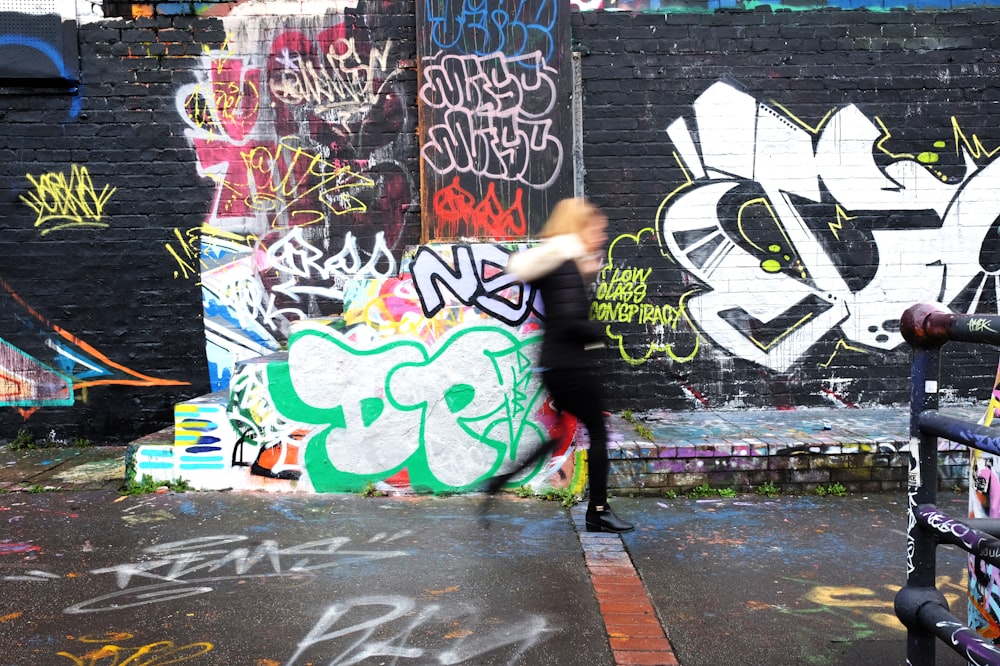 panning photography of woman walking beside wall with graffiti art