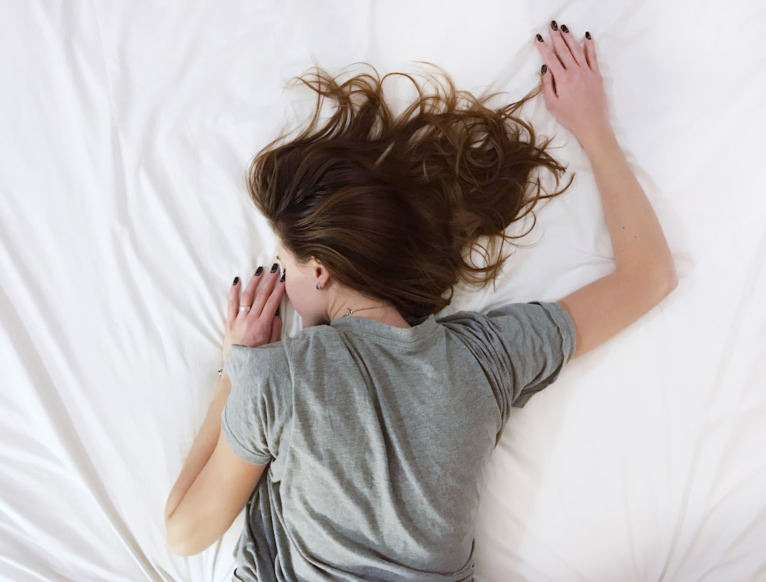 A woman with brown hair and a gray t-shirt lies face down on a white sheet
