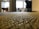 A close-up view of a textured carpet with a blurred background, suggesting an office or indoor environment. The carpet shows intricate weave patterns, and the space appears to be lit by natural light coming through a window.