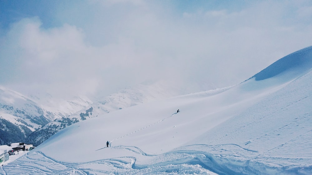 two people hiking on snow covered hill during day