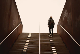 man in black jacket walking on brown wooden staircase