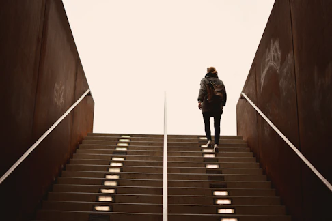 man in black jacket walking on brown wooden staircase