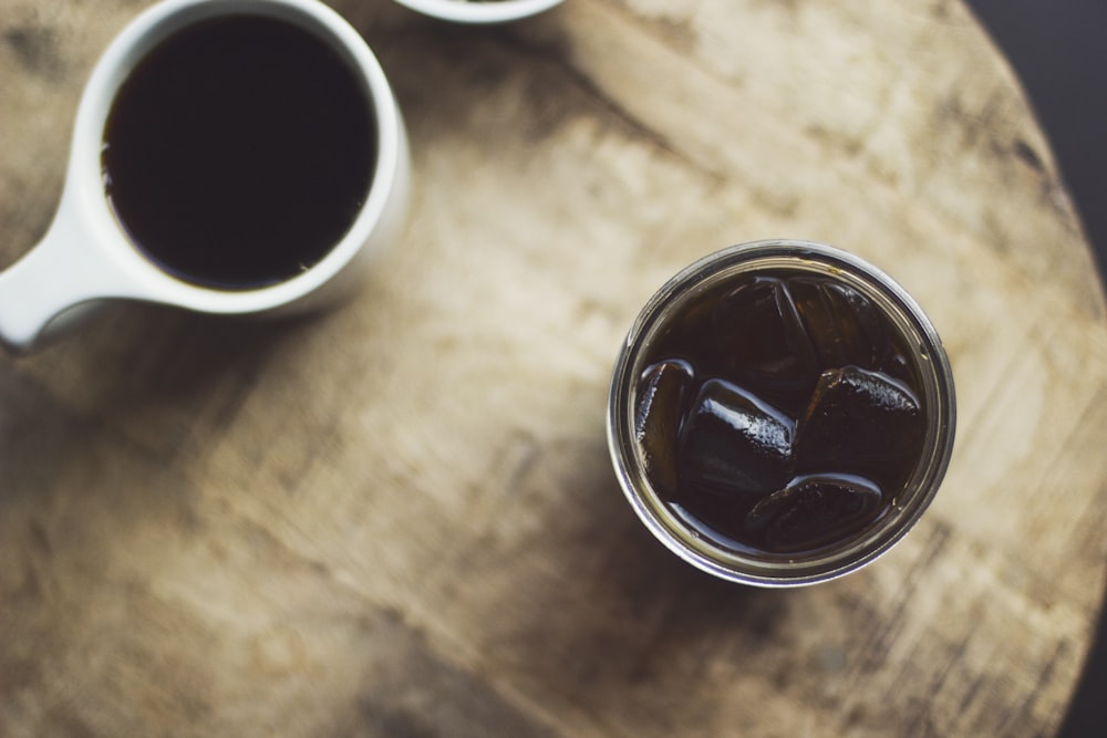 Taza redonda de cerámica blanca cerca de vaso de vidrio transparente lleno de líquido negro sobre la mesa