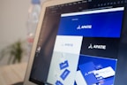 A computer screen displays a graphic design software with a brand identity project open, featuring multiple blue-themed design variations for a brand labeled 'APATIE'. The image includes different versions of the brand's logo and designs on a grid layout. The background shows a blurred bottle and some greenery out of focus.