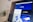 A computer screen displays a graphic design software with a brand identity project open, featuring multiple blue-themed design variations for a brand labeled 'APATIE'. The image includes different versions of the brand's logo and designs on a grid layout. The background shows a blurred bottle and some greenery out of focus.